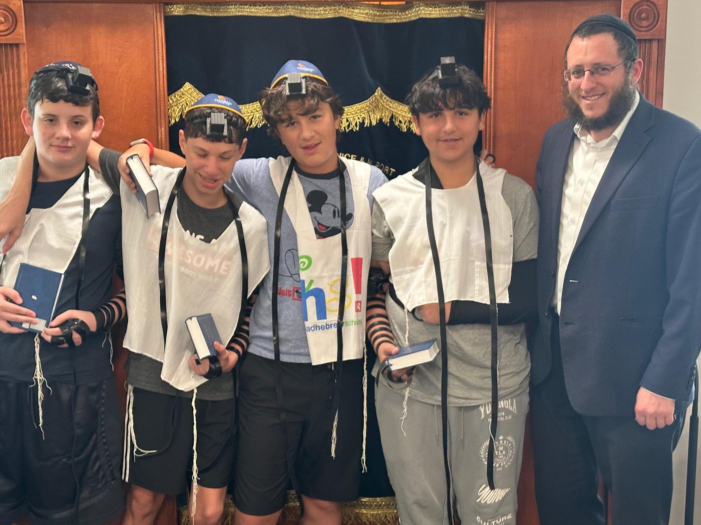 Four bar mitzvah boys wearing tefillin beside the rabbi in front of the open ark at Chabad of Venice