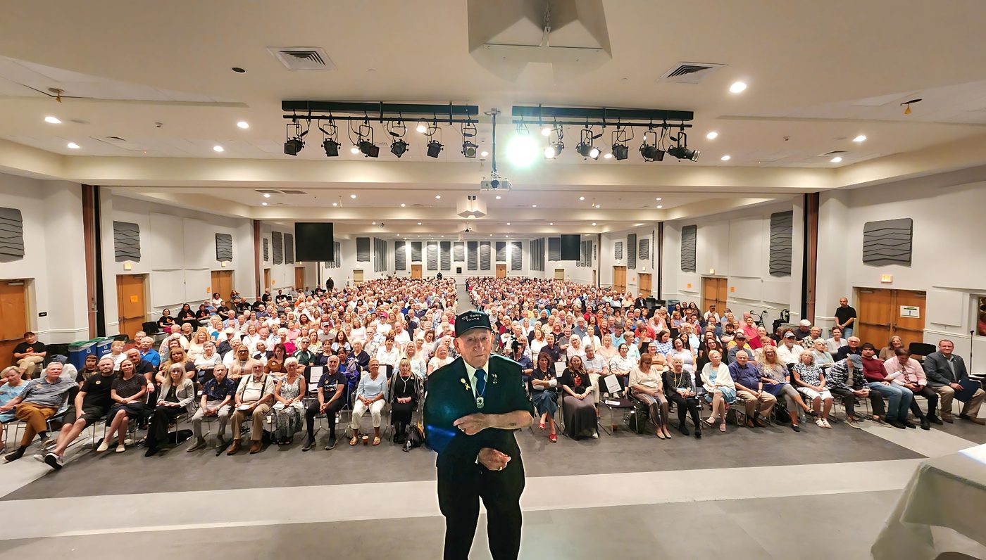 Joseph Alexander standing on stage before a packed auditorium at the Venice Community Center