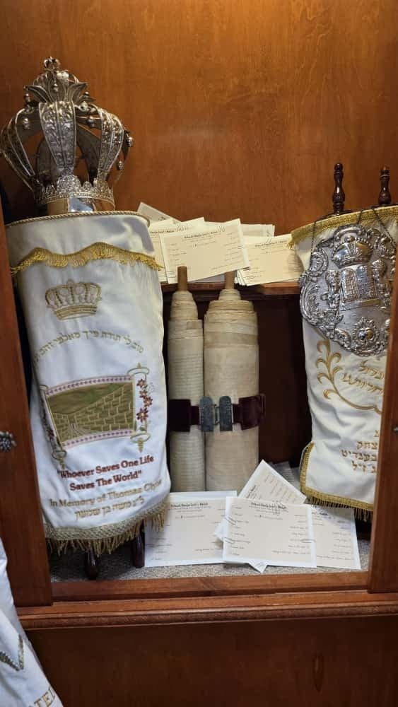 The restored Holocaust Torah resting in the open Aron Kodesh, surrounded by hundreds of handwritten mitzvah pledge cards