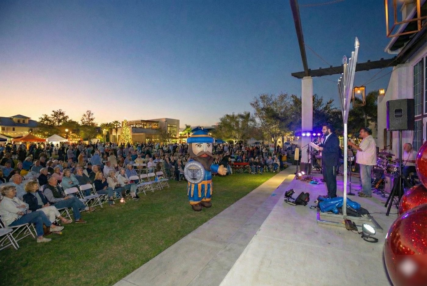 A large crowd seated at dusk for the Wellen Park menorah lighting, the stage lit and the band playing