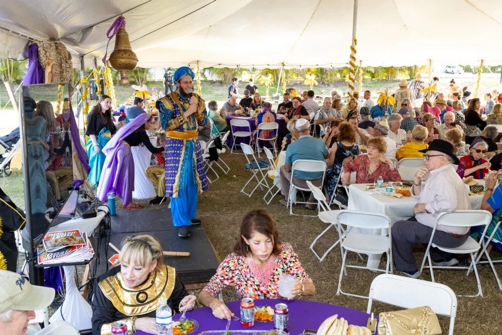 Guests in Persian costume filling a festive tent at the Purim in Persia celebration, with the stage program underway