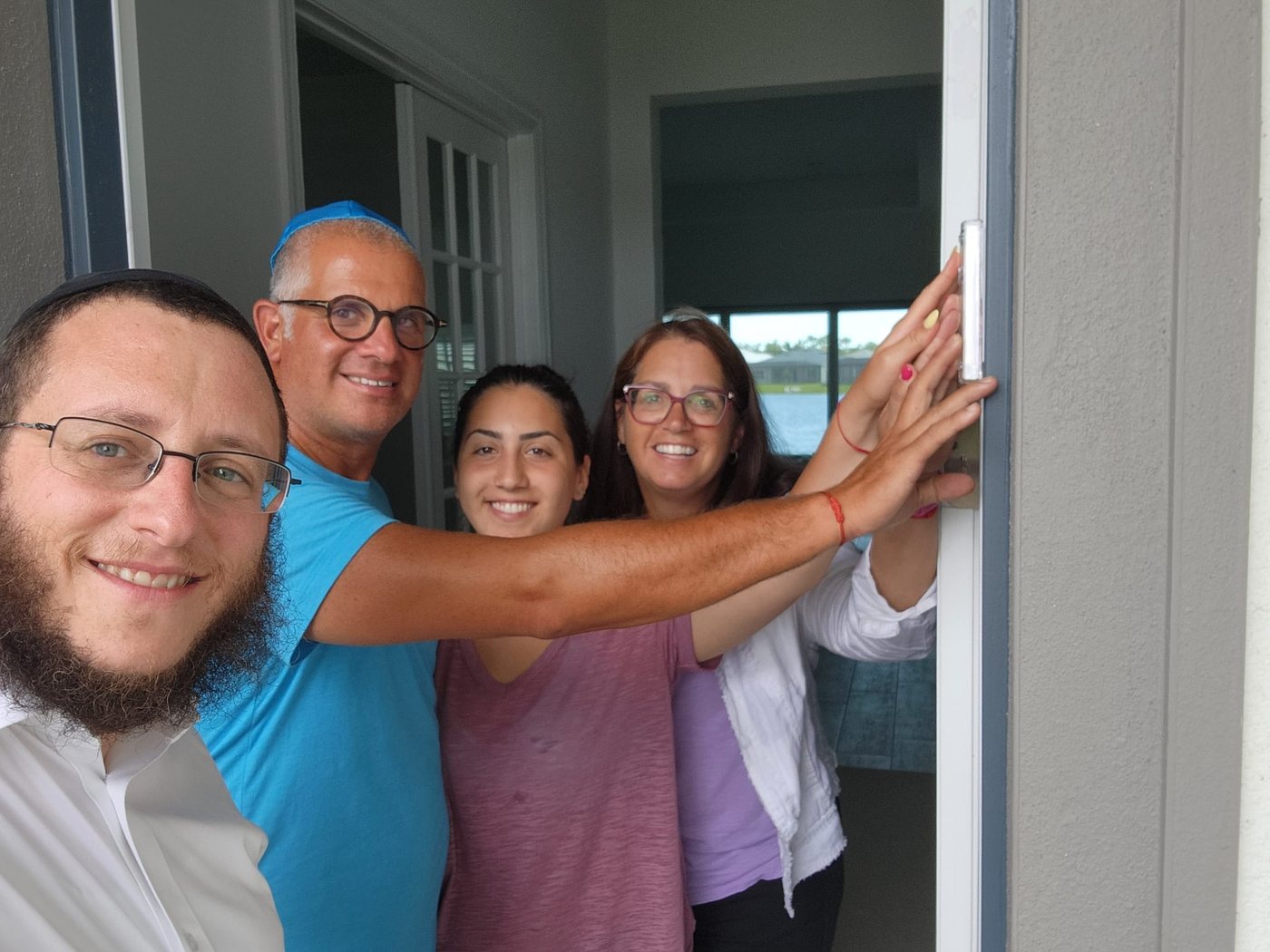 A family and their rabbi affixing a mezuzah together at their front door
