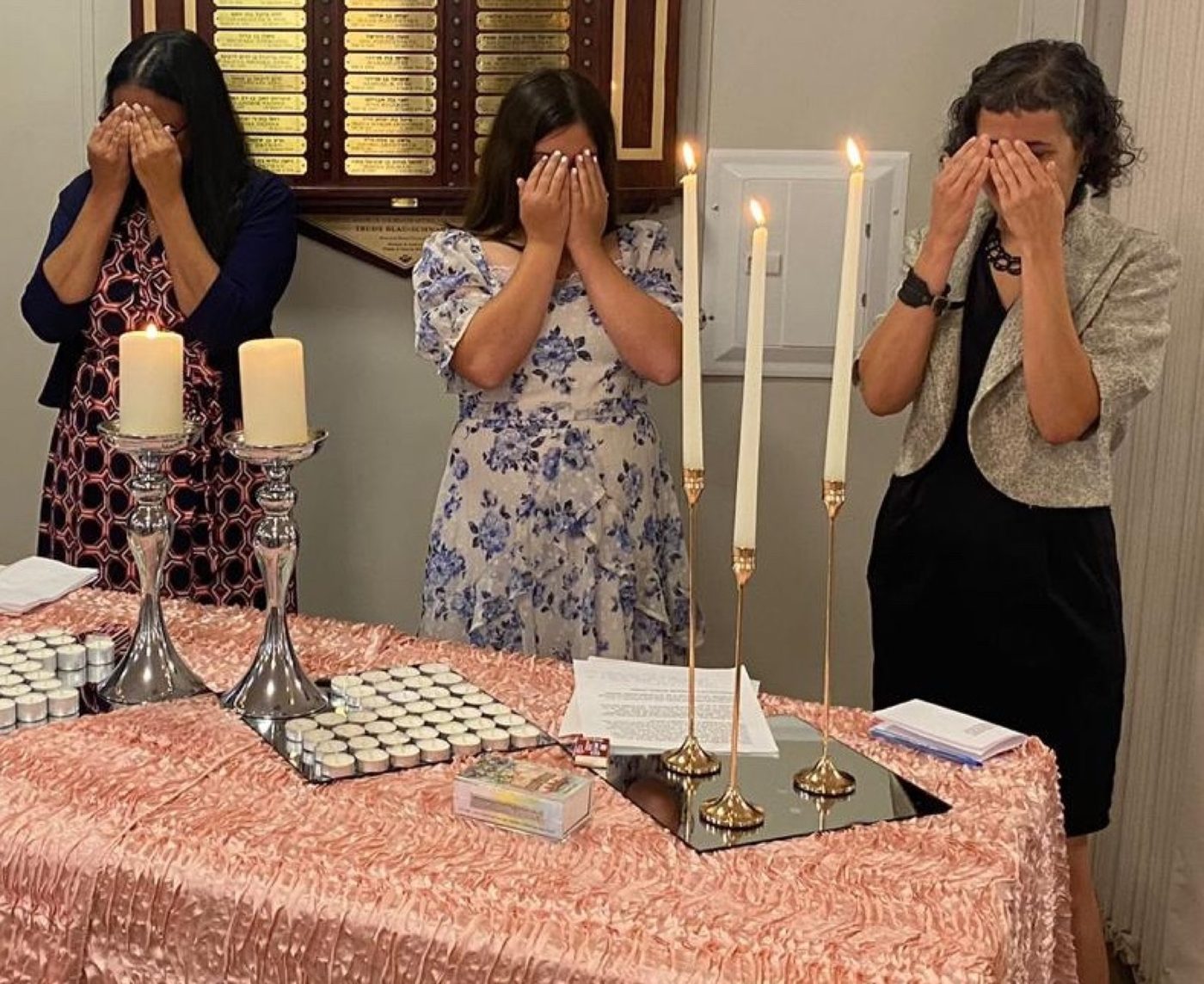 Three women covering their eyes over freshly lit Shabbat candles at Chabad of Venice