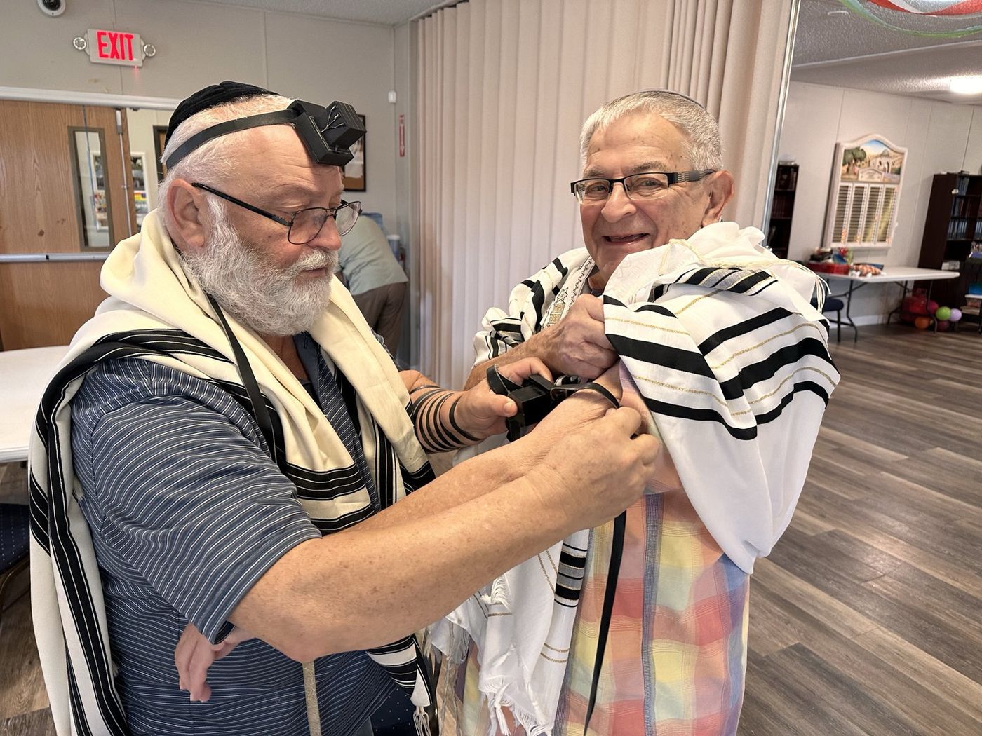 One man helping another wind the tefillin strap on his arm at Chabad of Venice