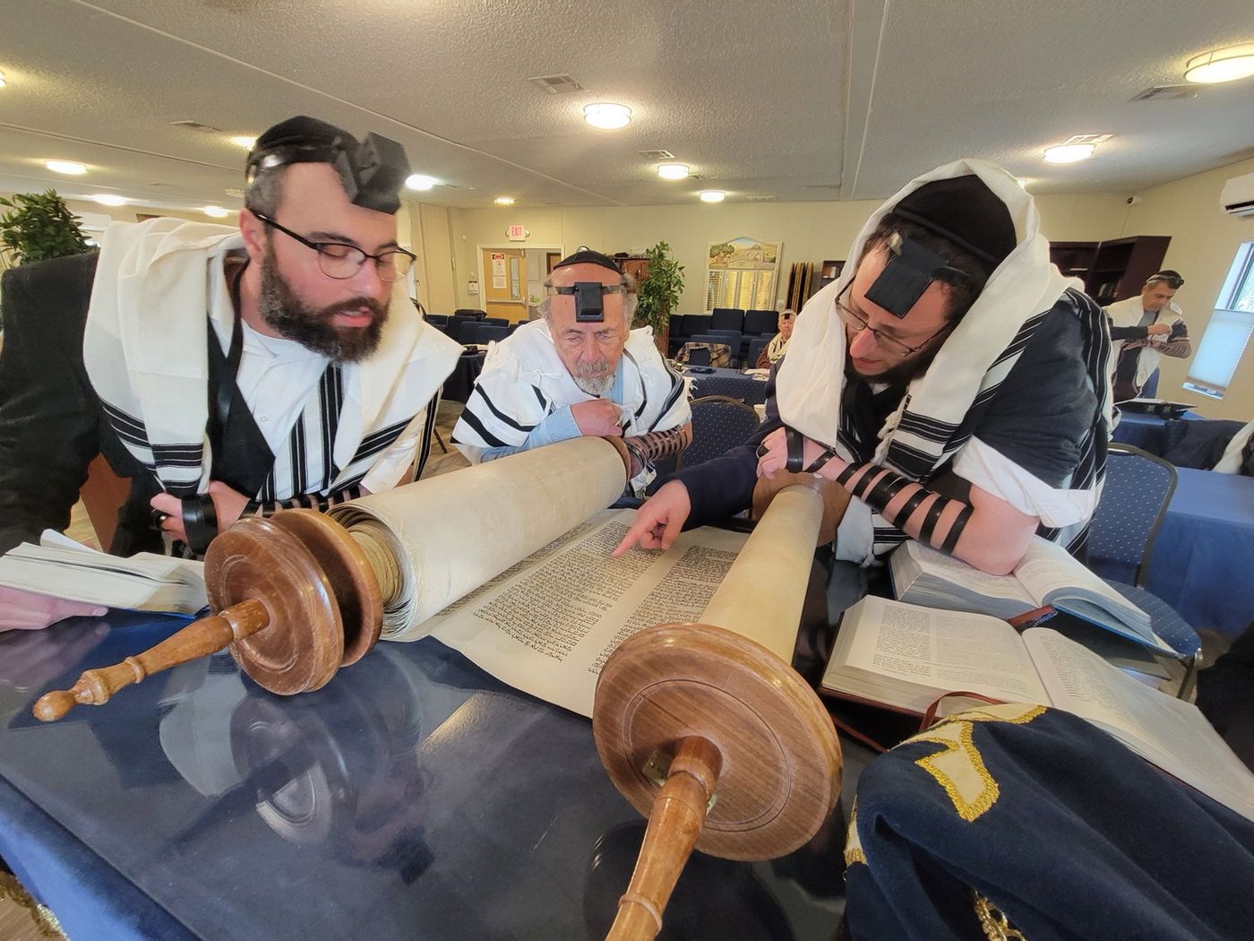 Men wearing tefillin gathered around an open Torah scroll at Chabad of Venice